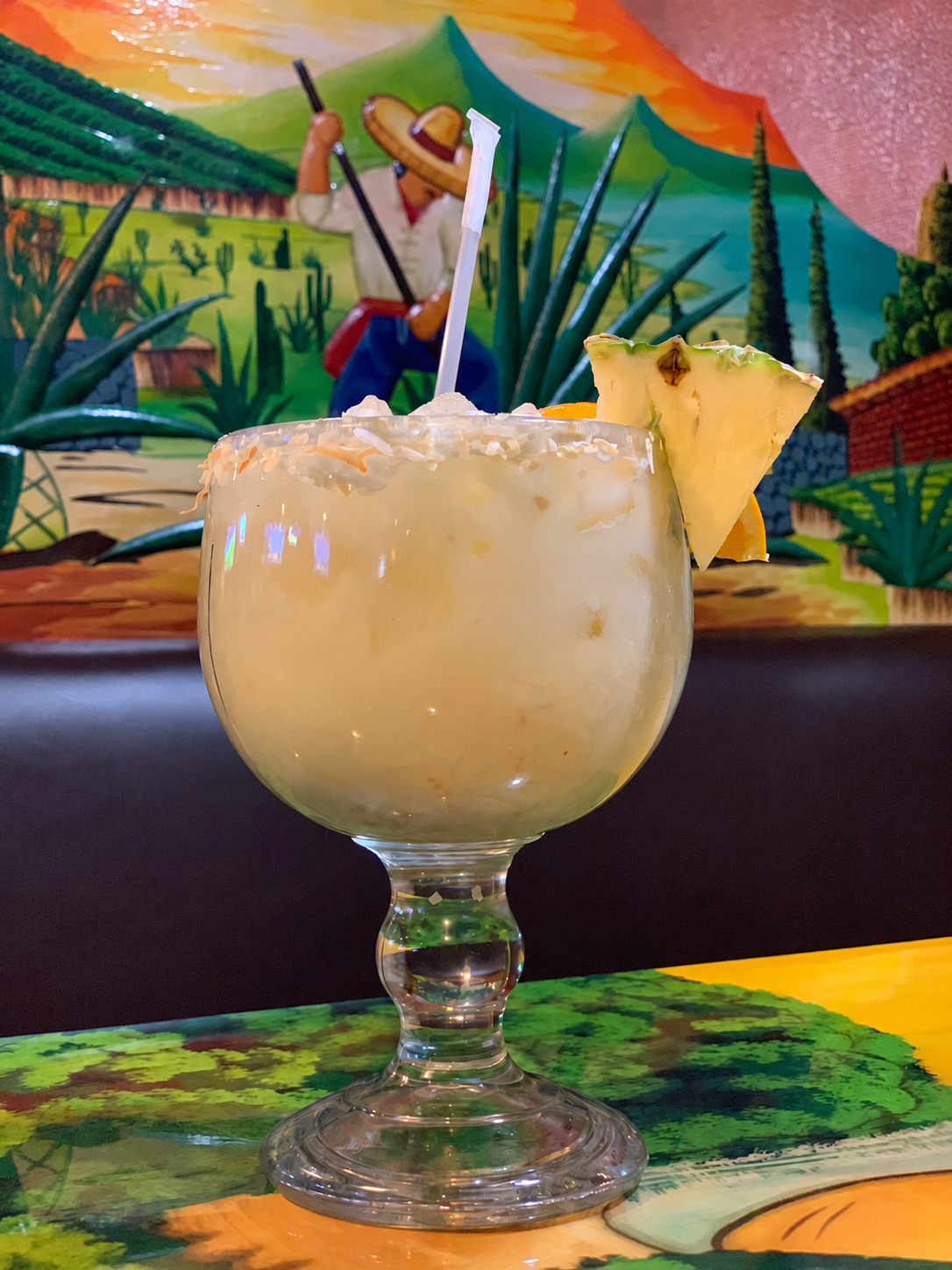 Pale tropical drink in a goblet with a coconut rim and pineapple garnish