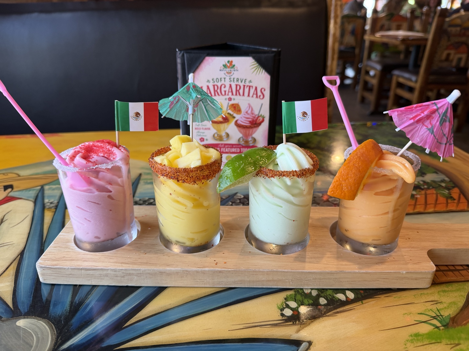 Four colorful margaritas on a wooden flight board