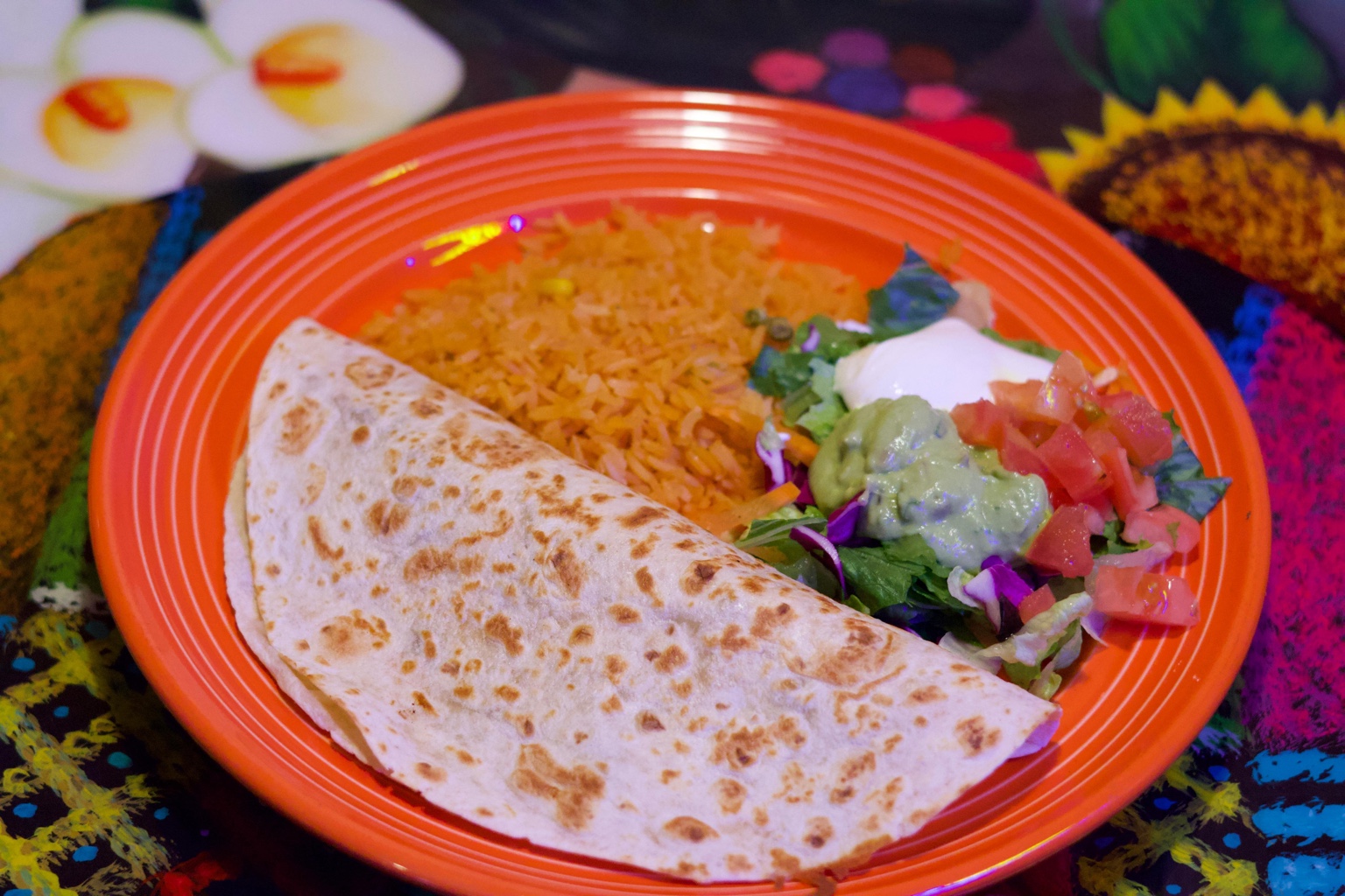 Quesadilla served with rice, guacamole, sour cream and salad on an orange plate
