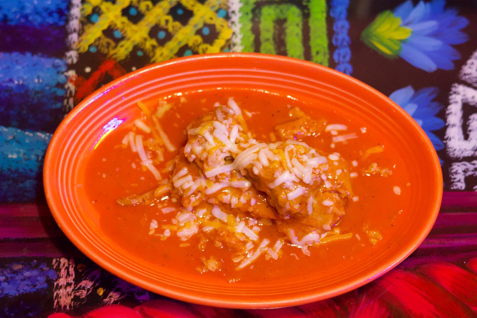 A bowl of red soup topped with shredded cheese