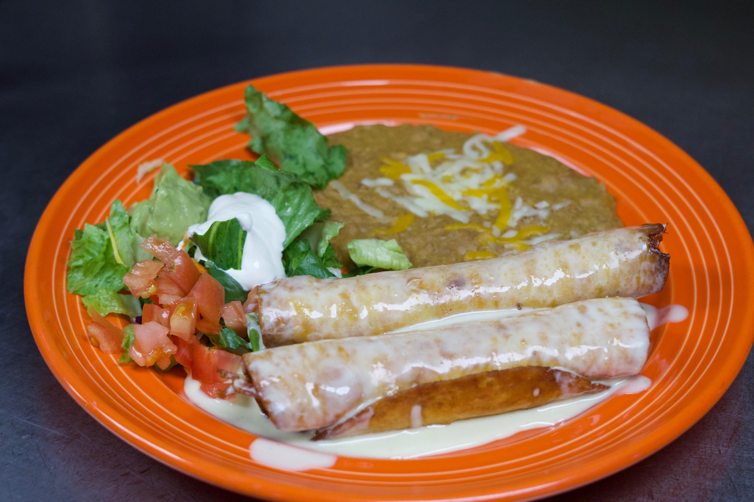 Rolled tortillas with cheese sauce, rice and salad on an orange plate