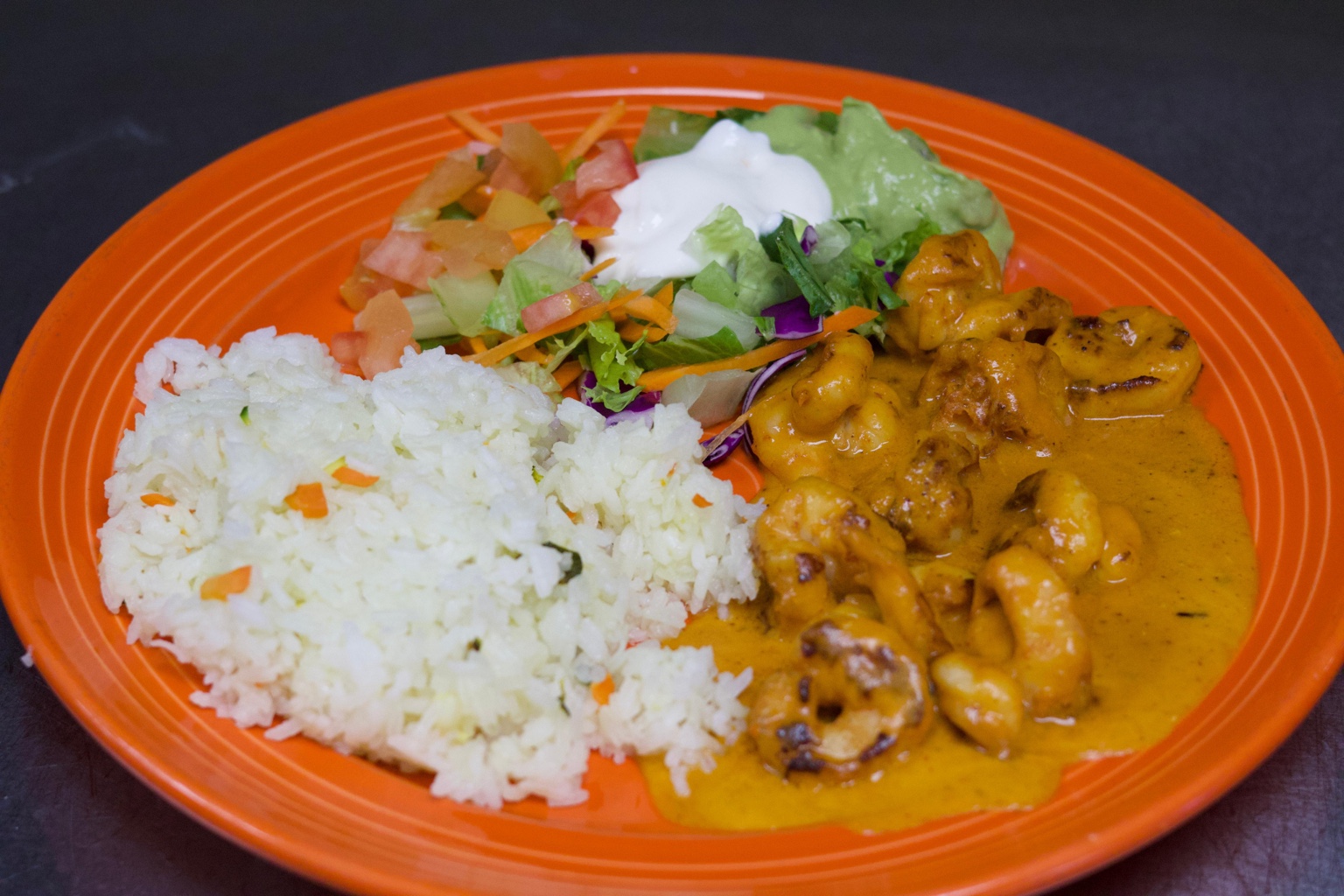 A sauced entrée served with white rice and guacamole salad